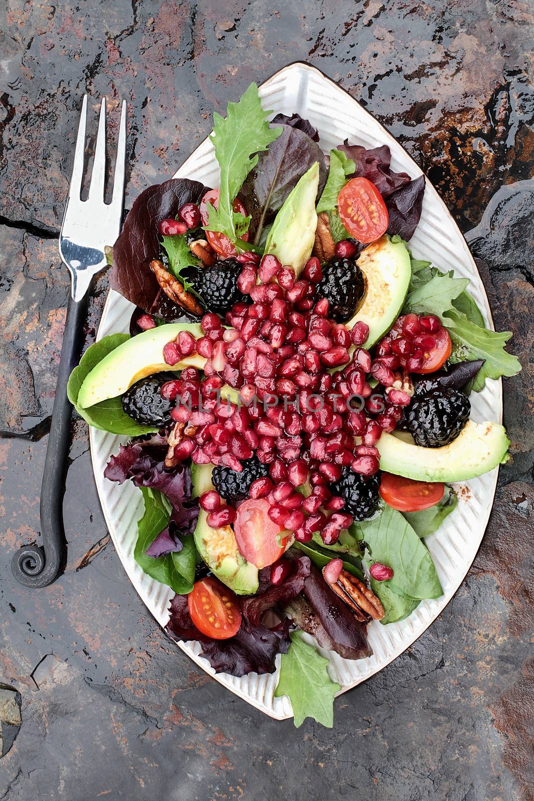 A healthy salad with pomegranate, avocado, tomatoes, almonds and argula lettuce over a rustic background. 