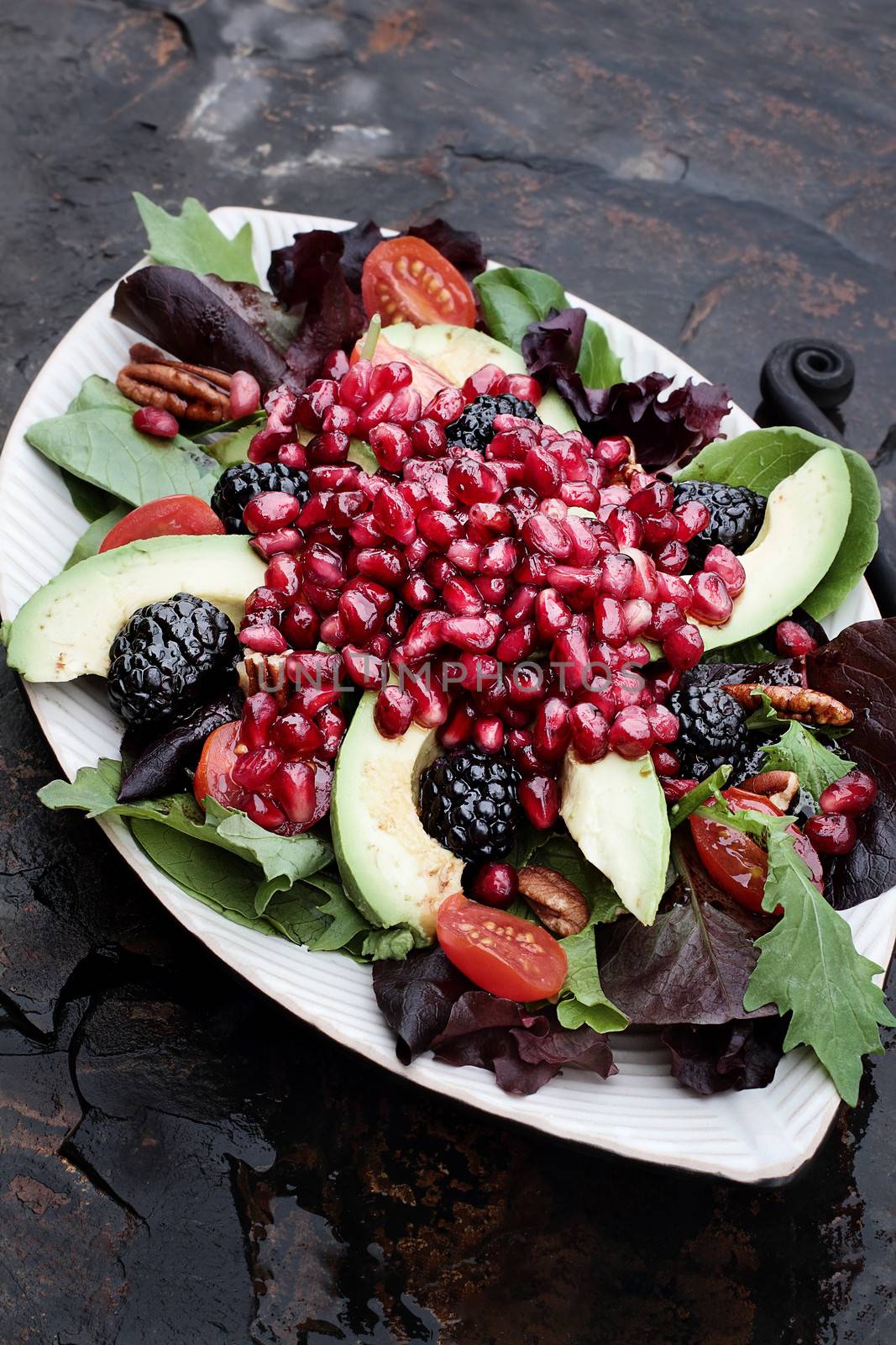 A healthy salad with pomegranate, avocado, tomatoes, almonds and argula lettuce over a rustic background. 