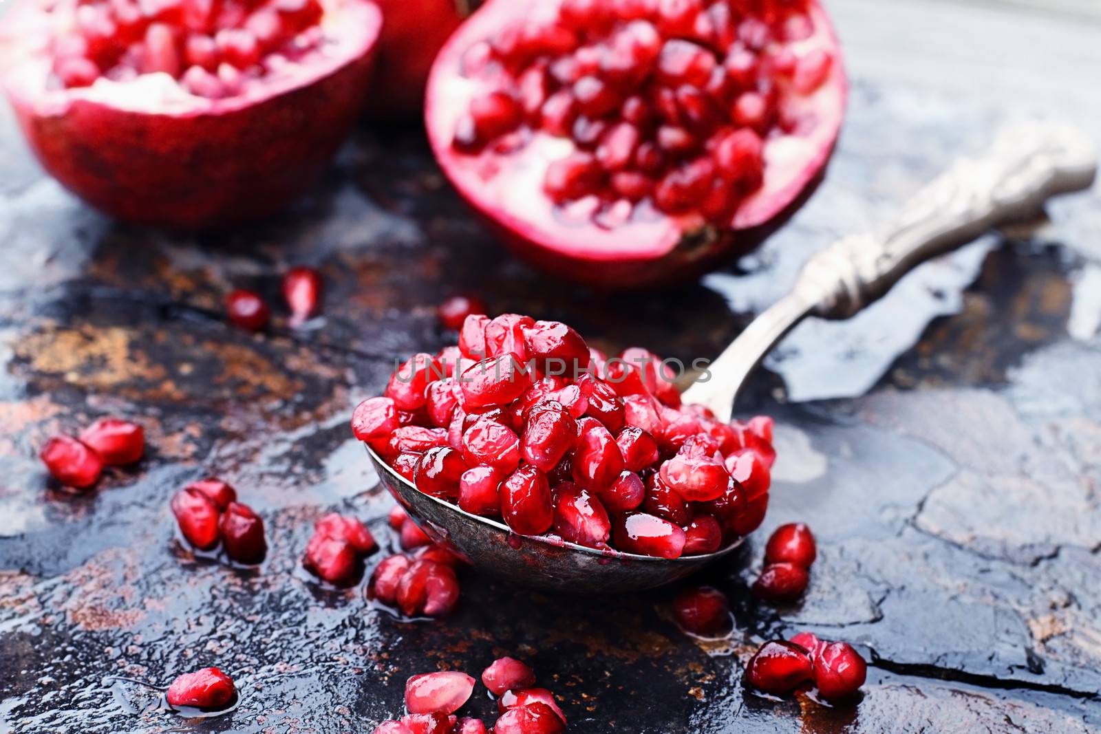 Pomegranate seeds in an antique silver spoon over a rustic background. 