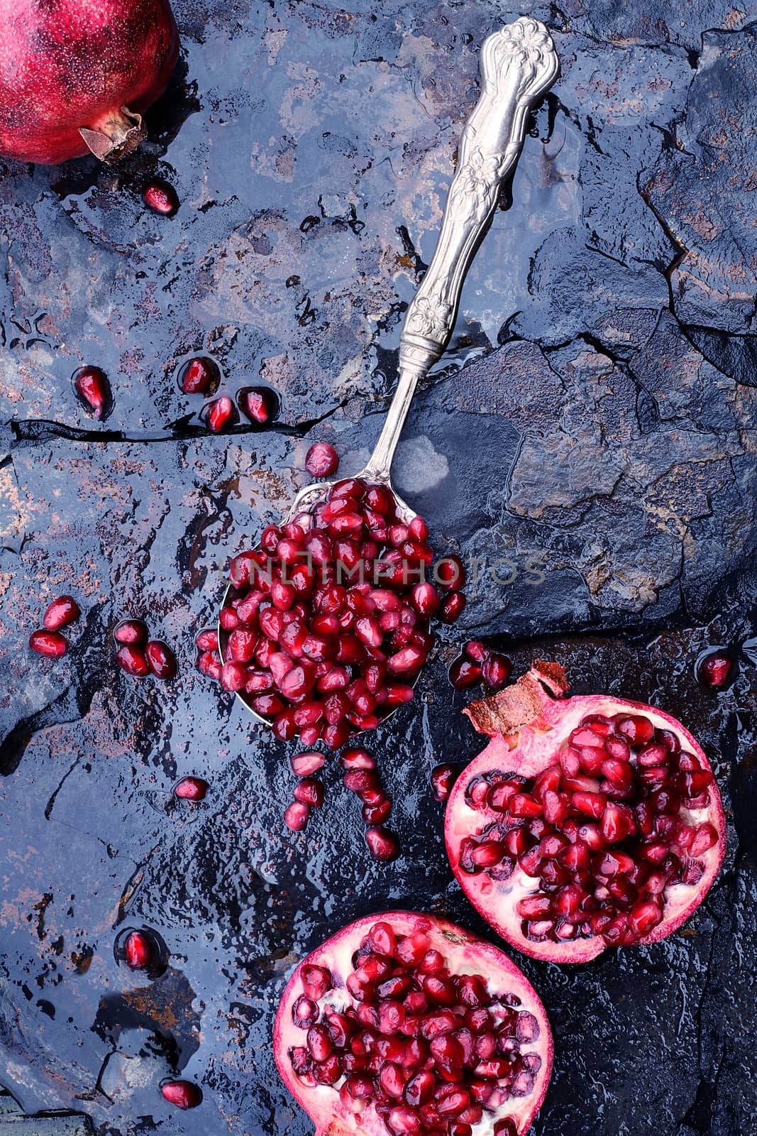 Pomegranate seeds in an antique silver spoon over a rustic background. 