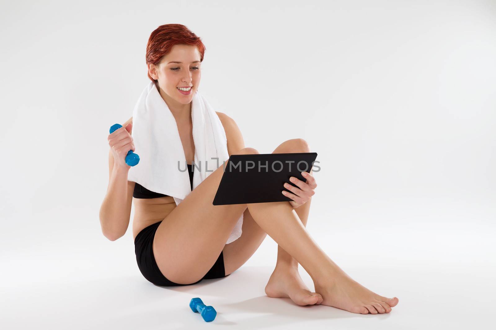happy woman getting fitness information from the internet with a tablet computer holding dumbbell