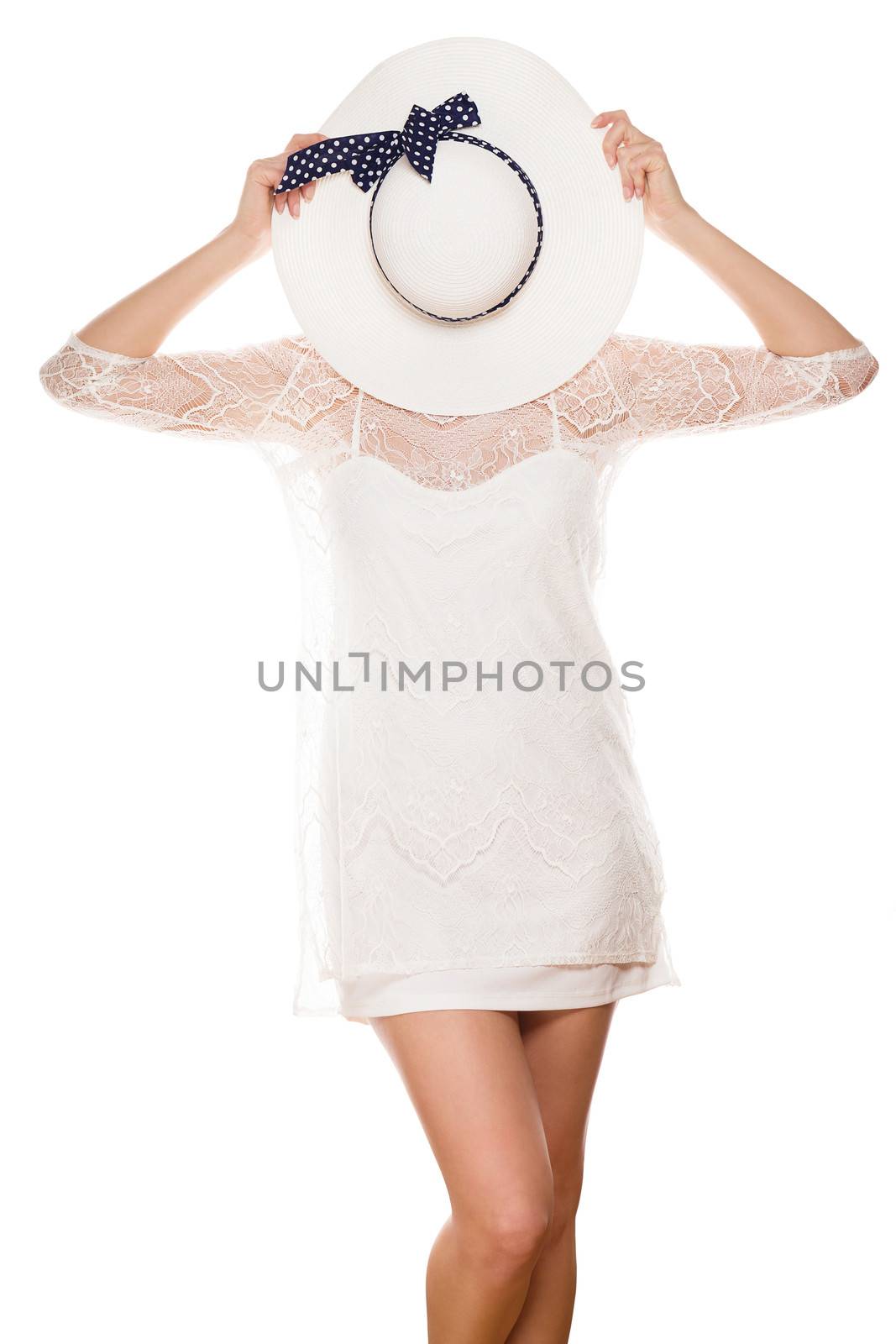 young woman in white dress hiding her face behind sun hat on white background