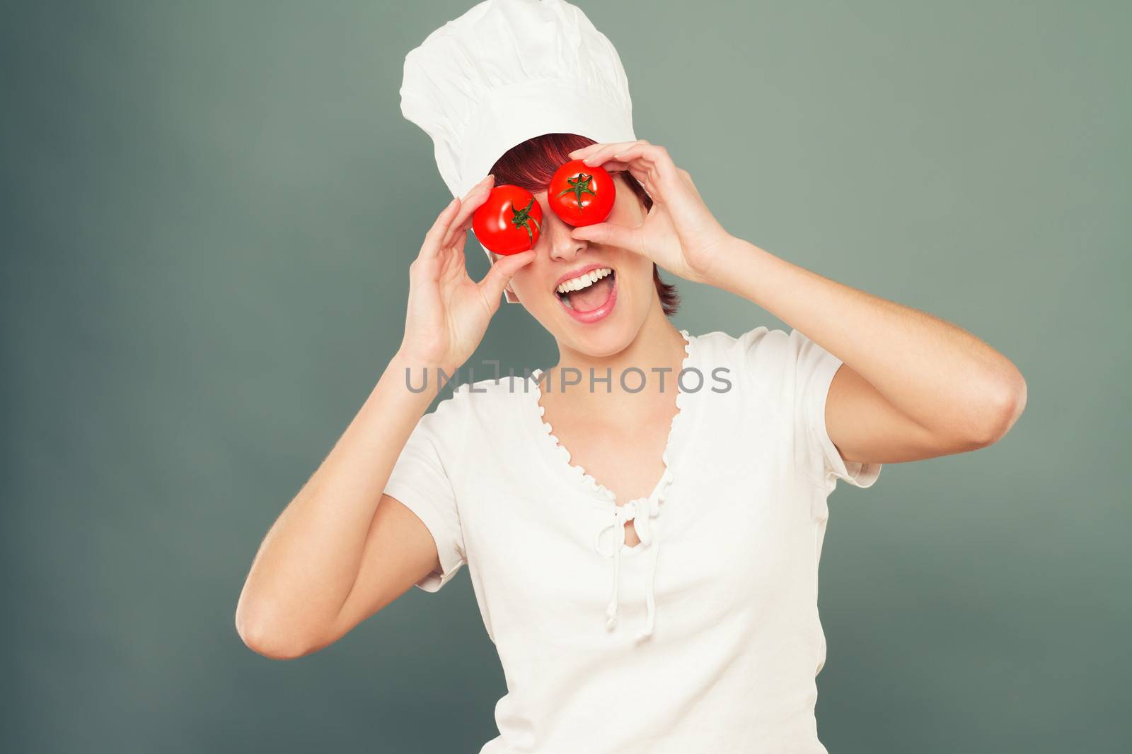 young happy female cook holding tomatoes on her eyes