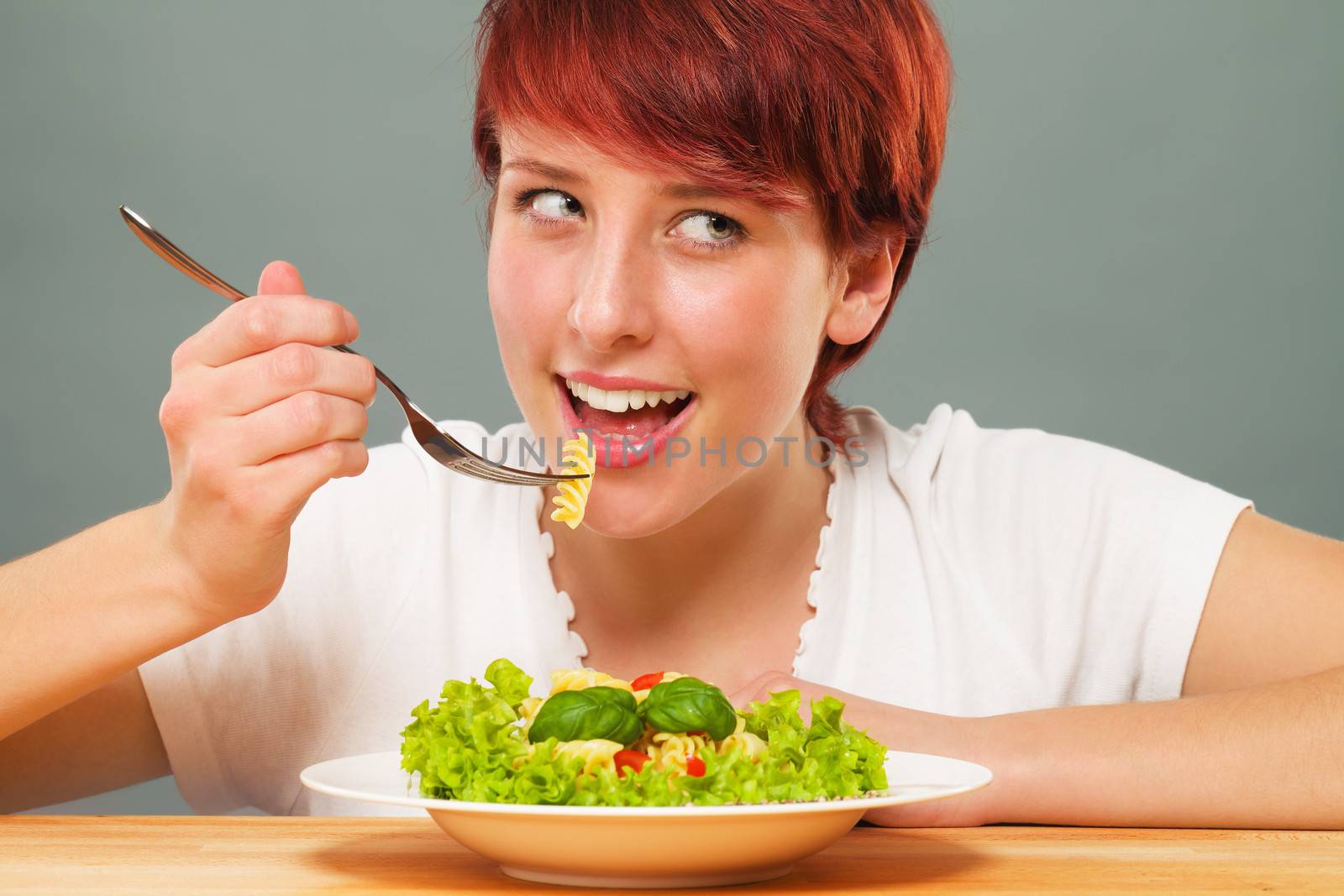young happy redhead woman eating pasta looking side