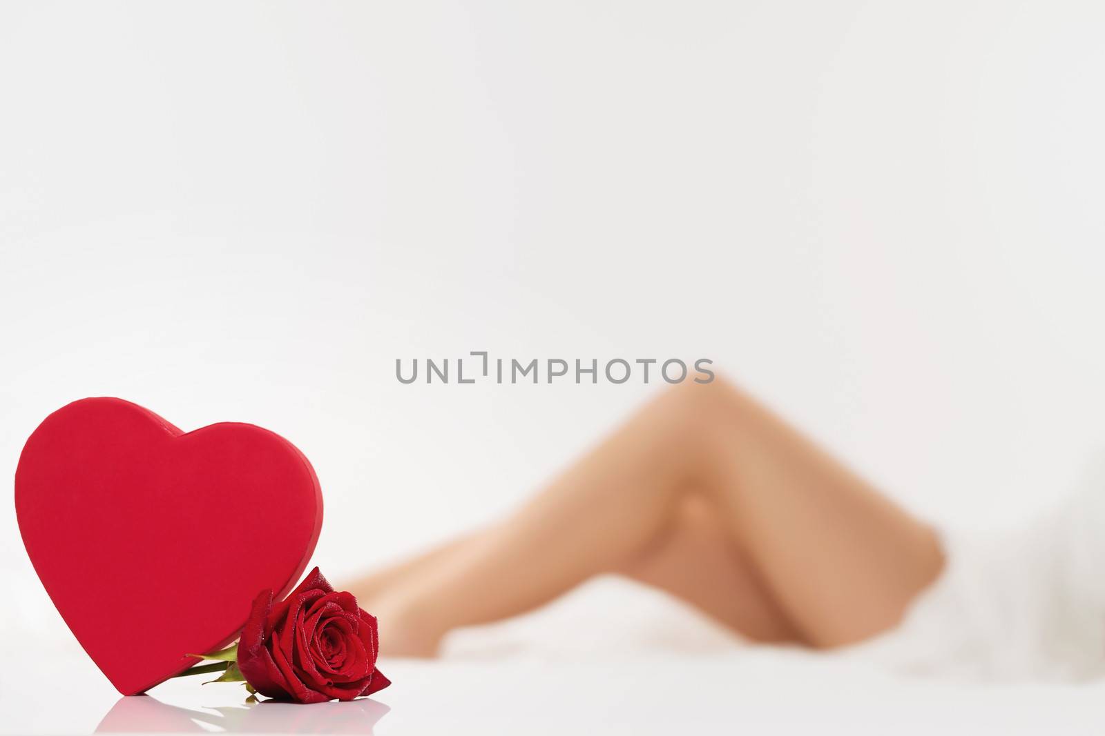 red heart and a wet red rose in front of beautiful legs from a woman