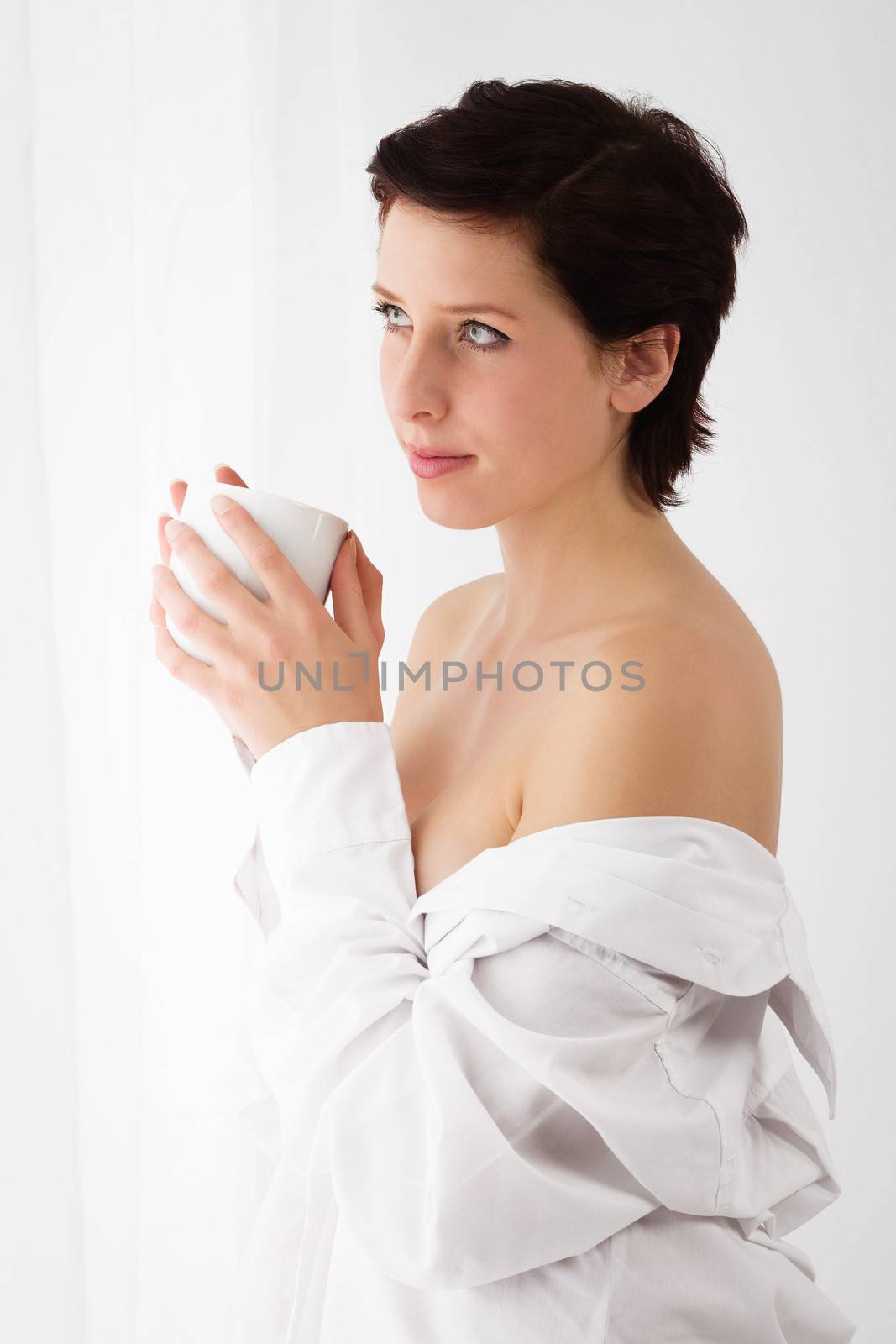 sensual woman at a window holding coffee wearing a white button down shirt