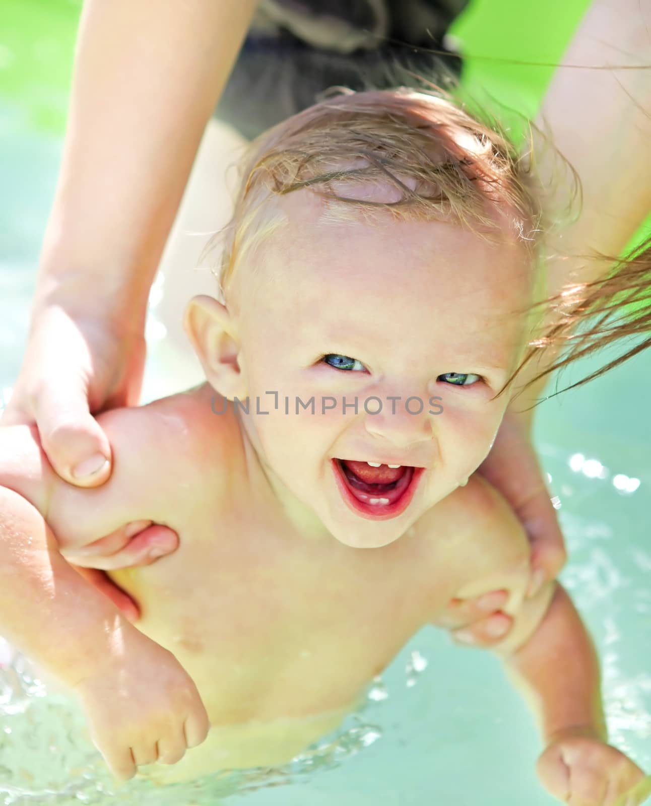 Parent bathing Cheerful Baby Boy in the Pool at Sunny Summer Day