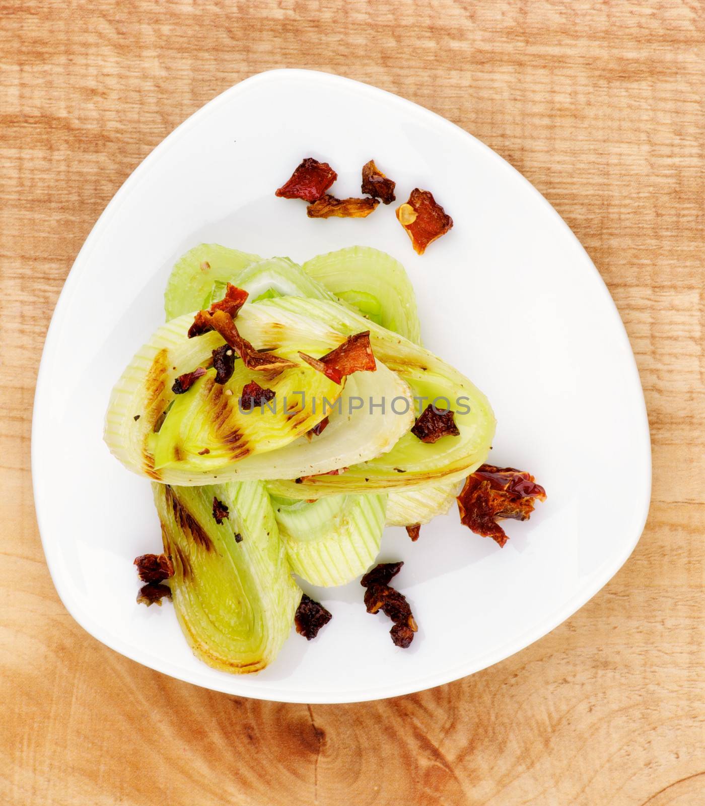 Tasty Roasted Leek with Fried Tomatoes and Paprika on White Plate closeup on Wooden background. Top View