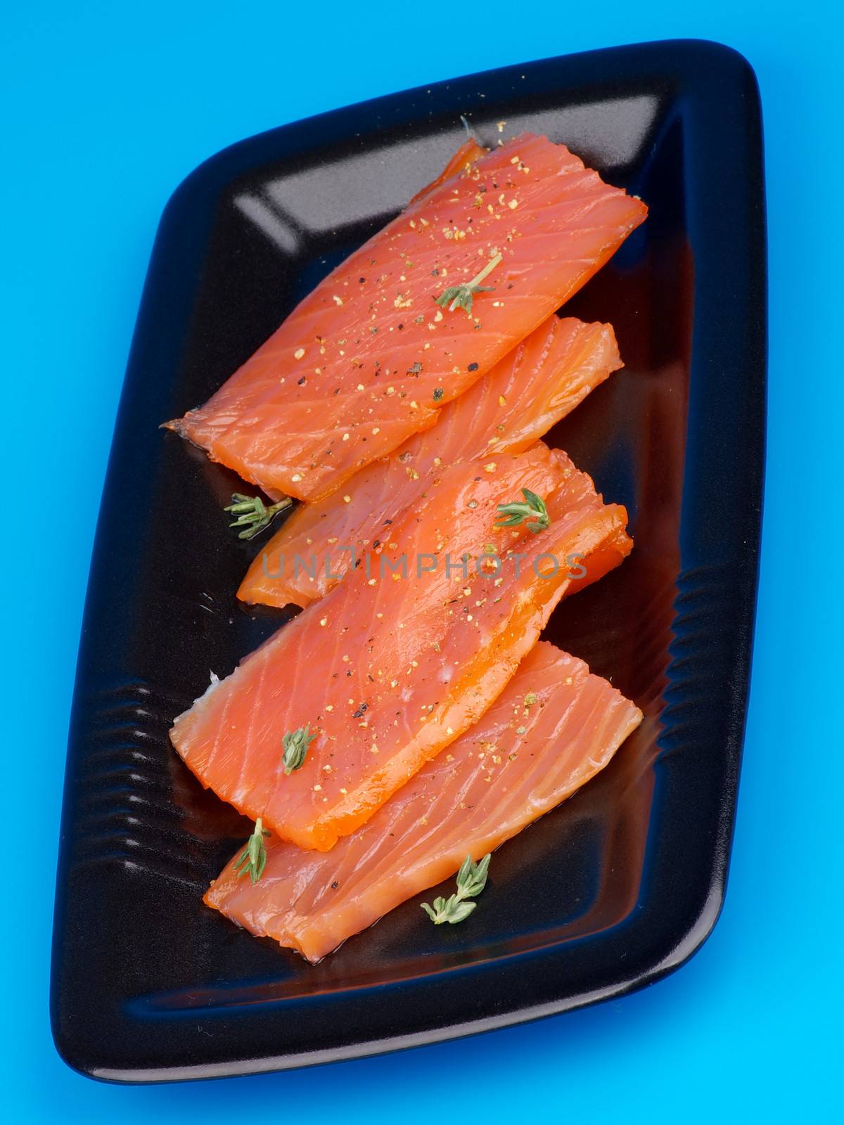 Slices of Delicious Smoked Salmon on Black Plate closeup on Blue background
