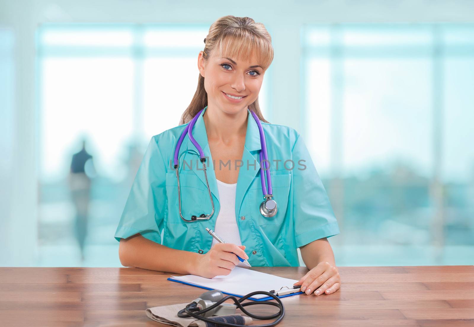 beautiful female doctor sitting at table and writing in clipboard