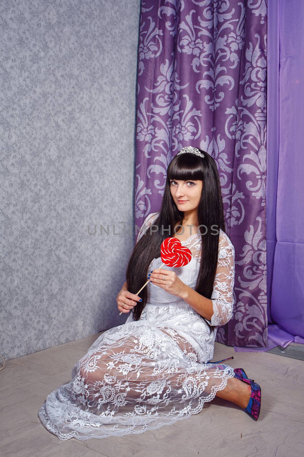 Attractive young girl sitting on the floor and holding a heart-shaped lollipop