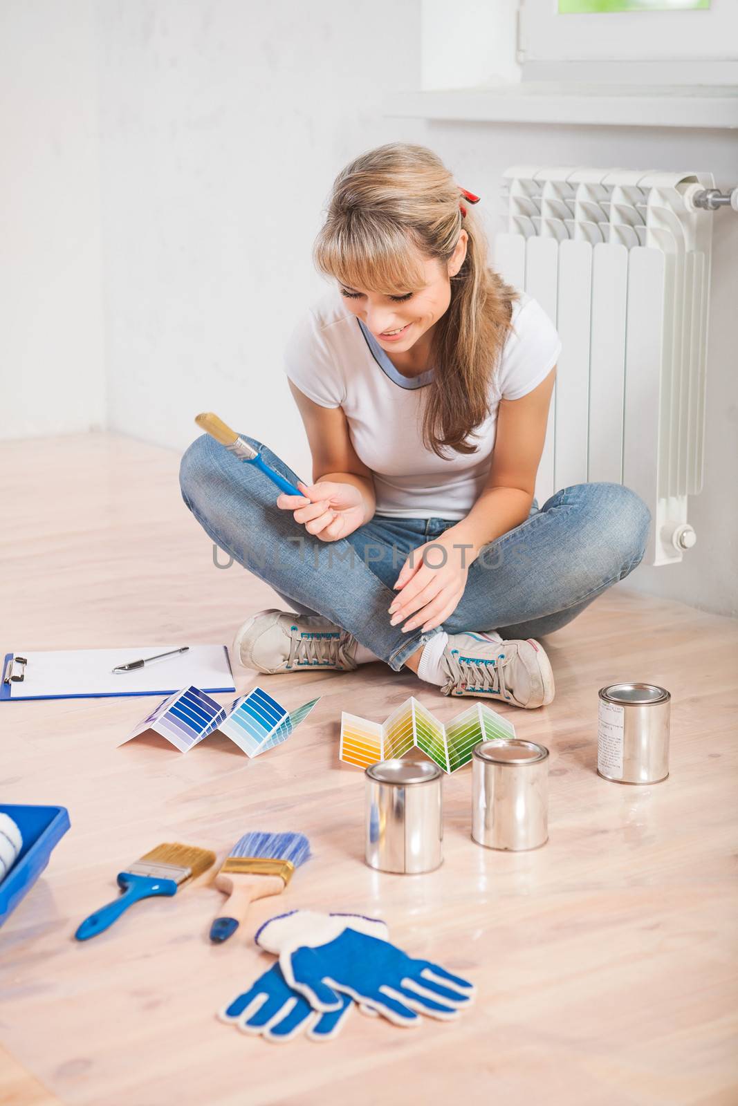 young female painter sitting on floor holding paintbrush and see in color palette