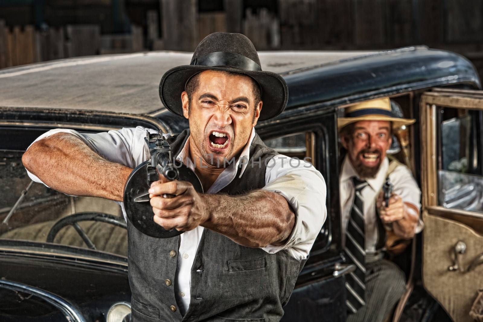 Angry mobsters firing submachine gun near antique car