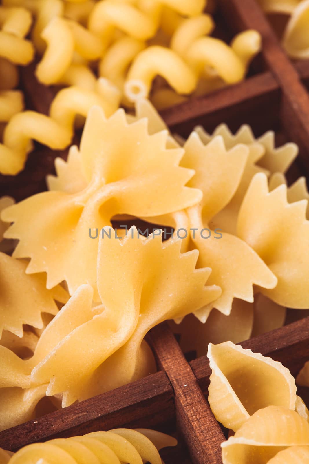 Various pasta  types in the wooden box on the table. Close up farfalle