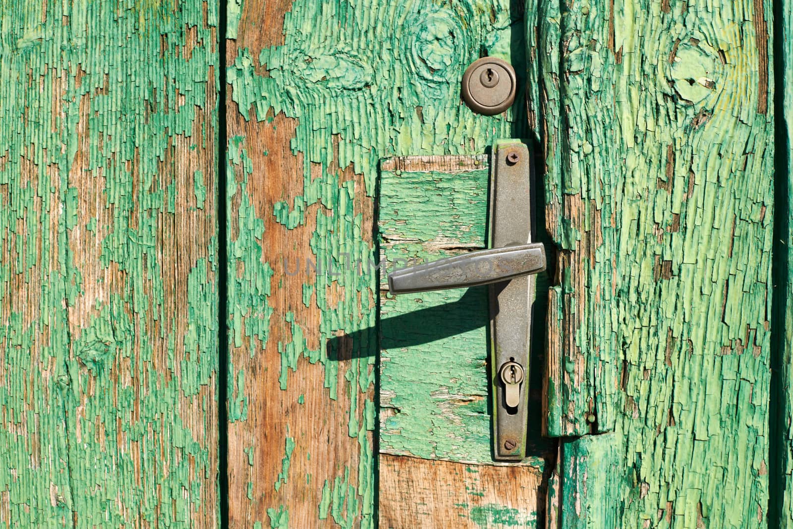 Old door handle on wooden door background with green ckracked paint 