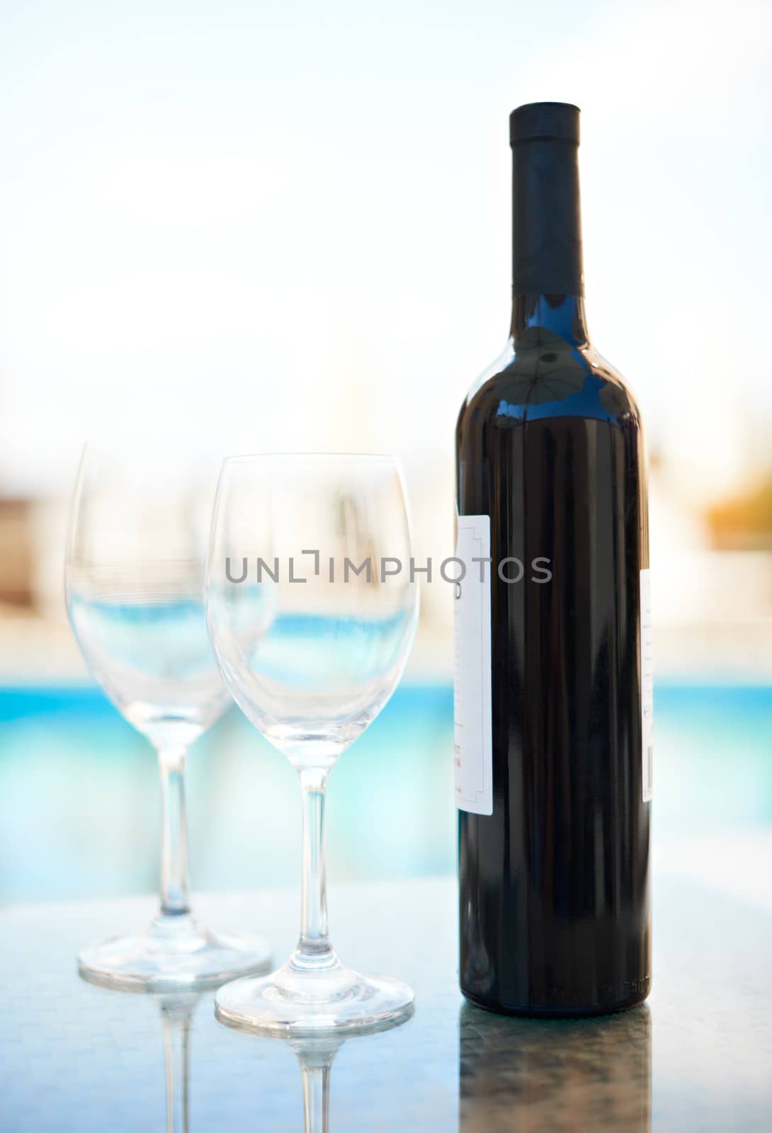 Bottle of red wine and two glasses near a blue water