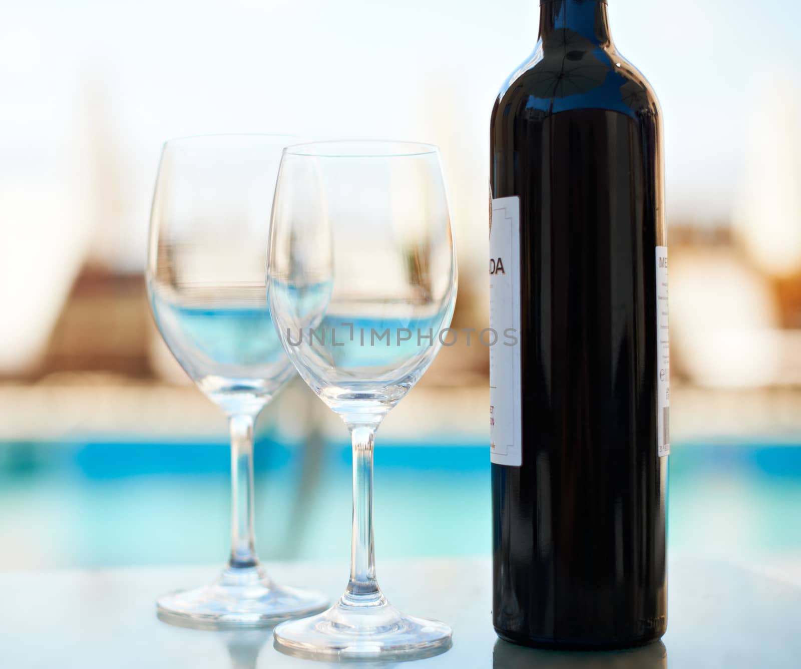 Two glasses and bottle of red wine near blue sea water