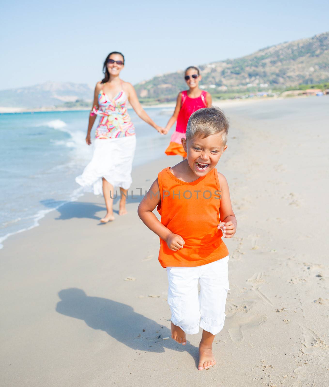 Adorable happy boy with sister and mother running on beach