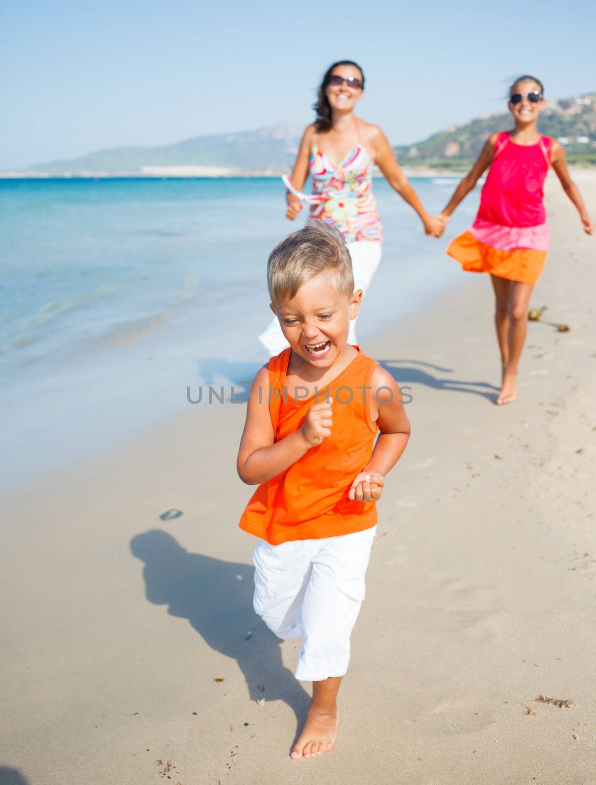 Adorable happy boy with sister and mother running on beach
