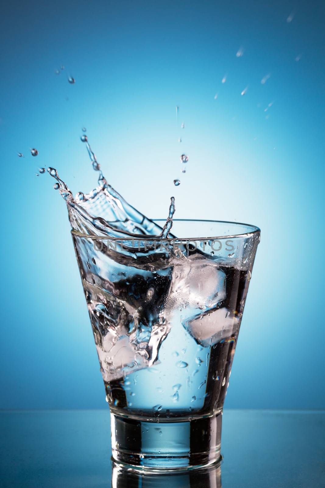 Ice cube splashing into a glassl of water. Blue background