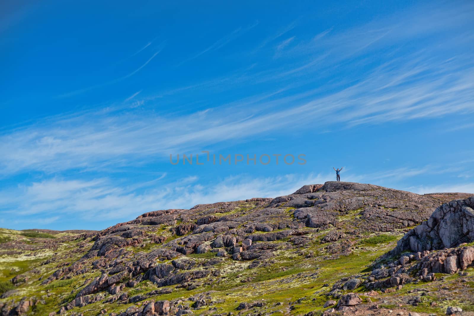 Man with a backpack on a mountain spread wide his hands in the summer against a blue sky with clouds