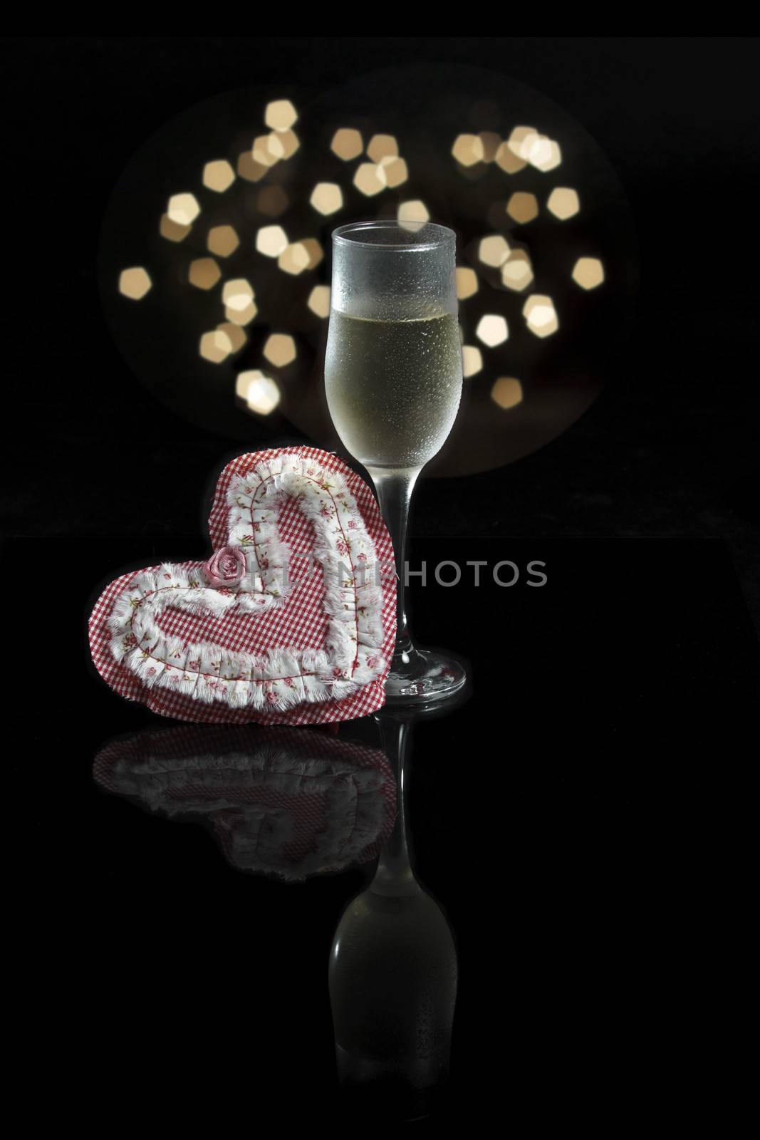 A glass of champagne, a heart made in patchwork and Christmas Lights on a black background