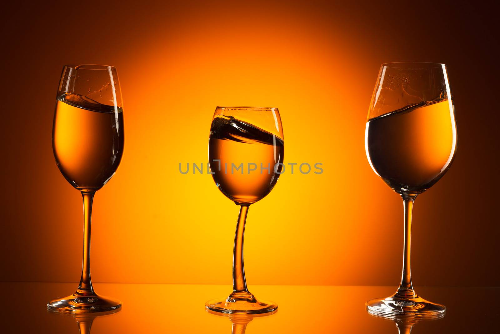 Three glasses on orange background with the liquid. On the background of orange light spot.