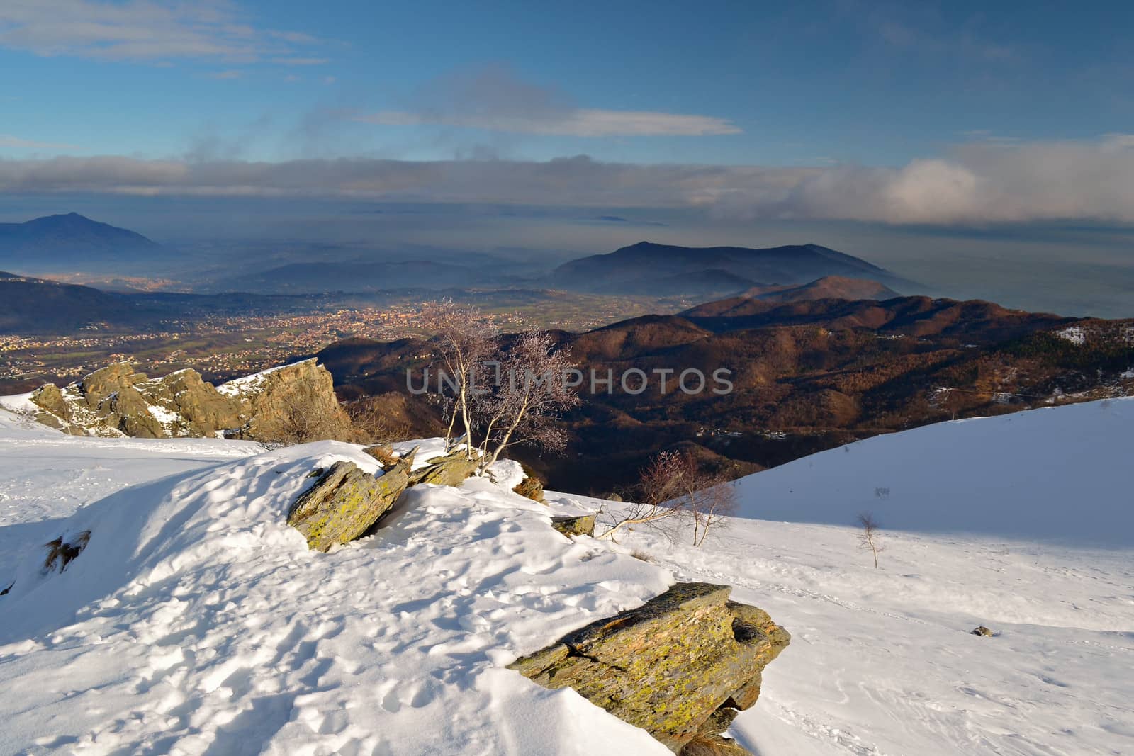 Winter landscape at sunset overlooking the smoggy valleys and villages below. Italian Alps.