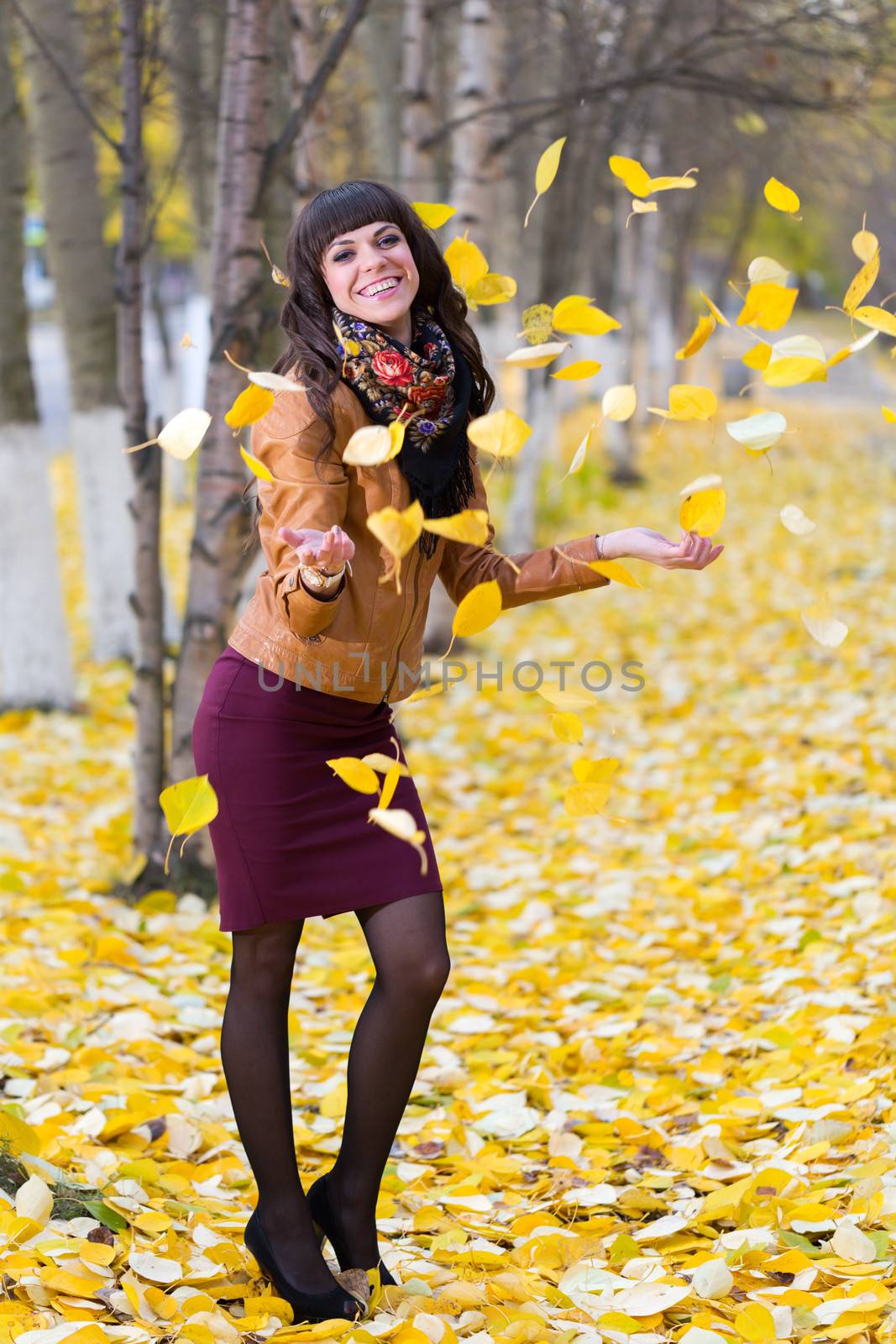 Glamorous girl throws up yellow leaves on the autumn alley