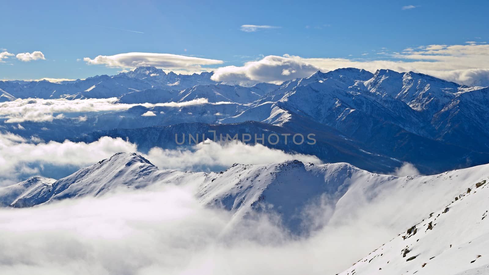 Aerial view of the alpine arc in a winter scenery with foggy valleys below. Italian Alps.
