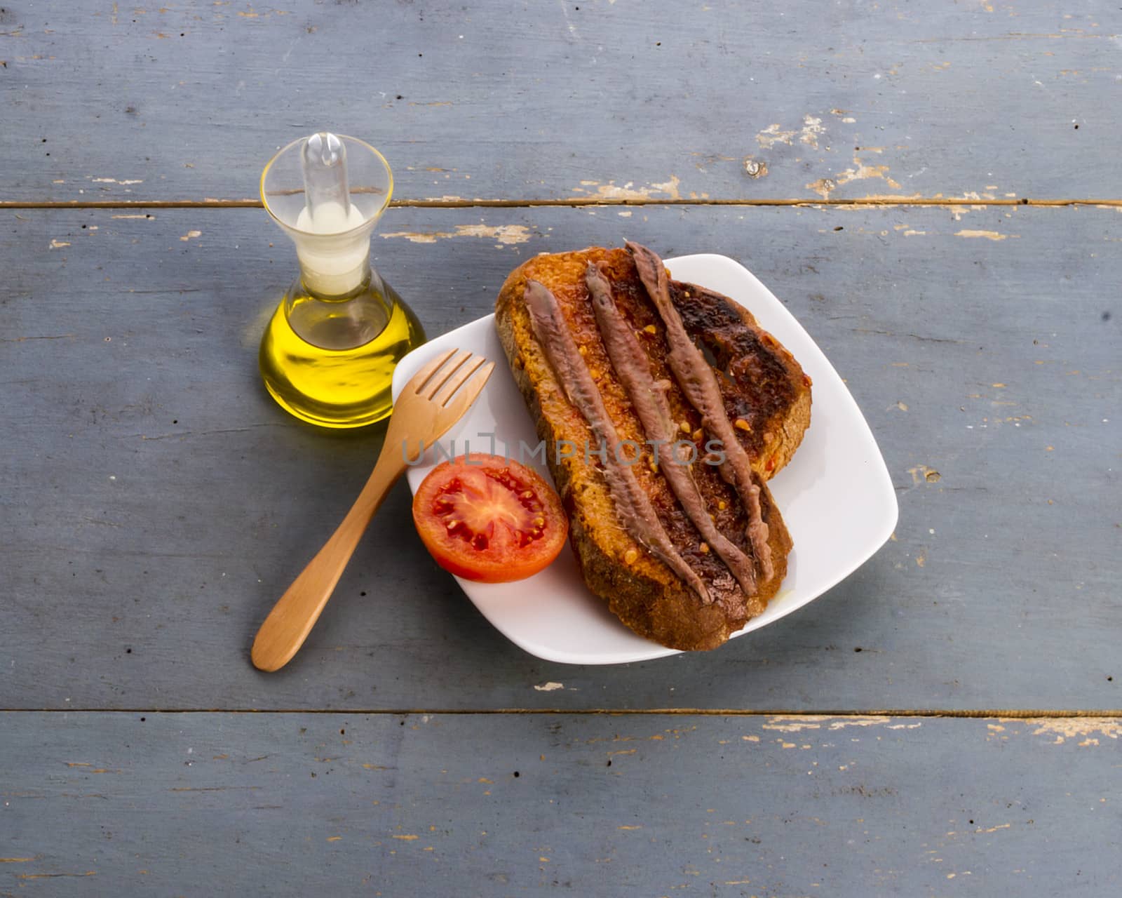 Still life with a catalan 'pa amb tomata' (bread or toast with tomato, salt and olive oil) with anchovies, on and old blue table