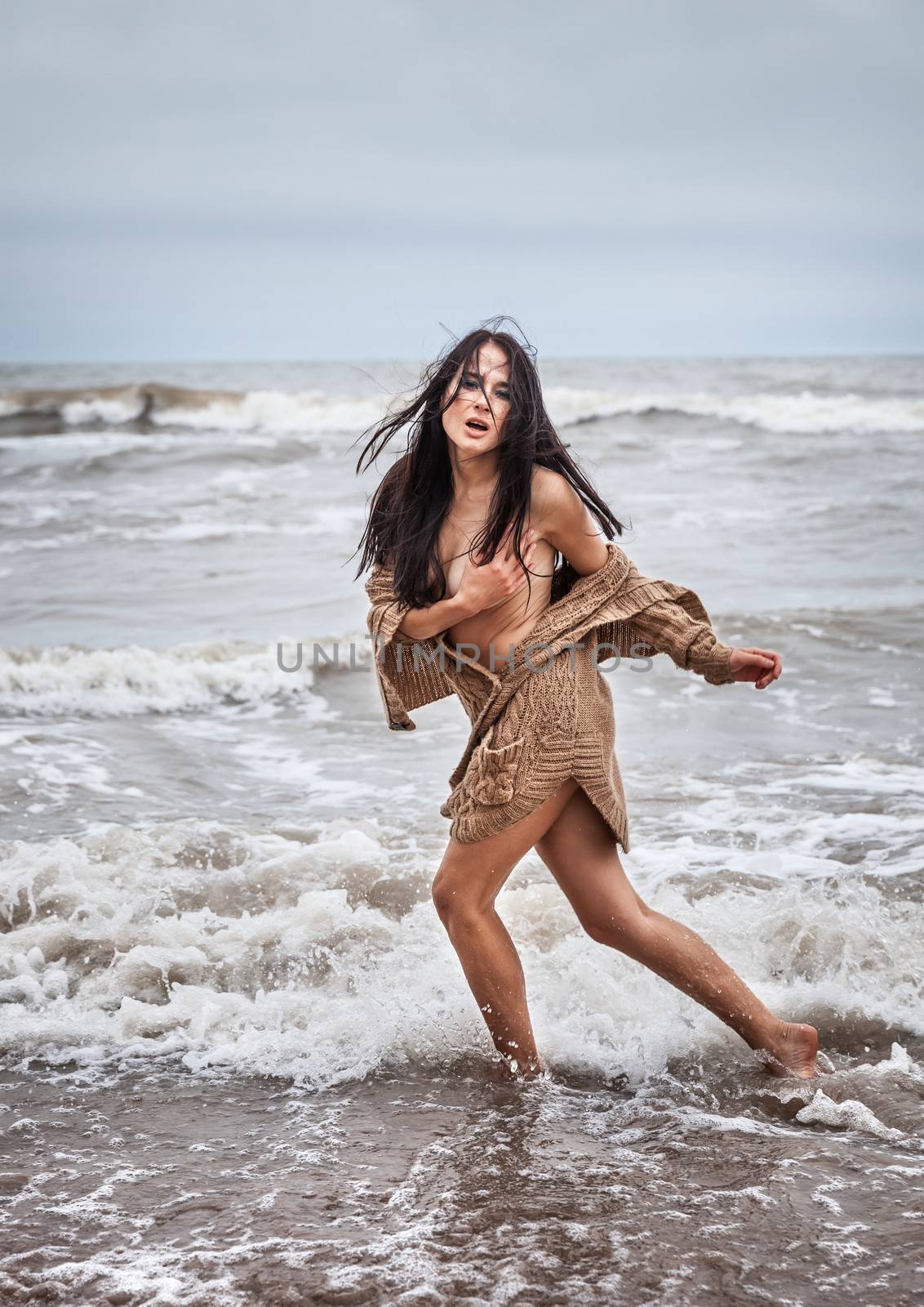 Beautiful young seminude woman in the cold sea waves