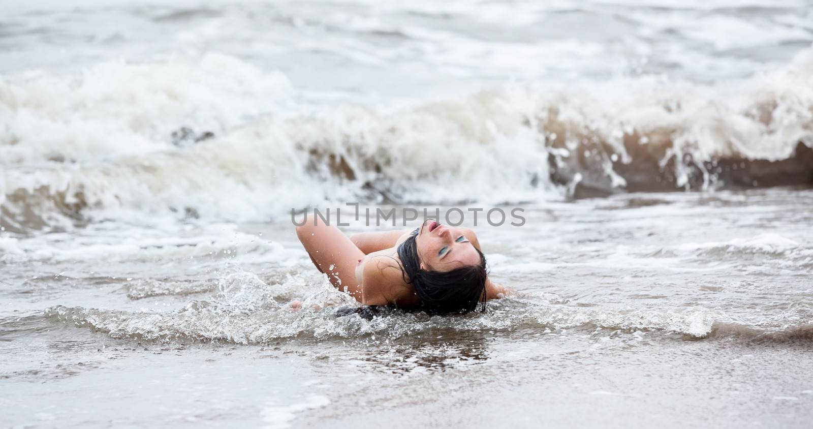 Beautiful young seminude woman in the cold sea waves