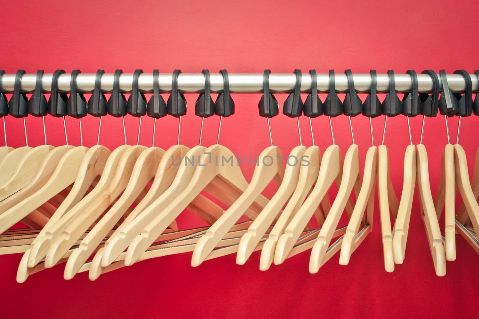 Wooden clothes hangers on a rail in front of a red wall