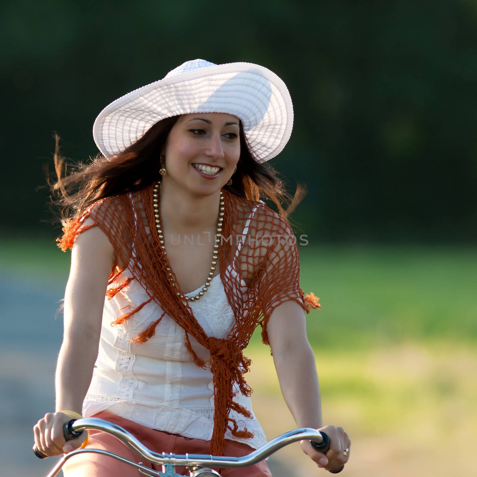 Woman in orange skirt and white hat riding on a retro bike in meadow view from the front
