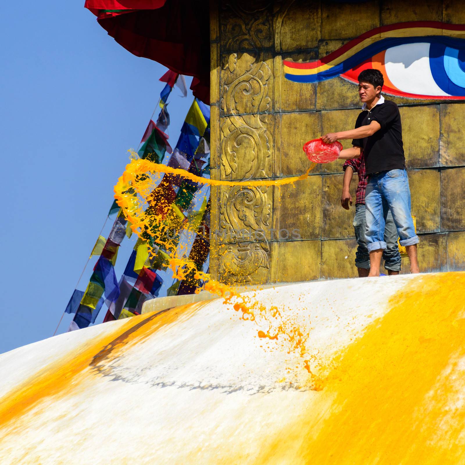 KATHMANDU, NEPAL - JANUARY 27, 2014: A man throws orange paint on Boudhanath Stupa as part of the renovation and painting work which will cost four million Nepalese Rupees.
