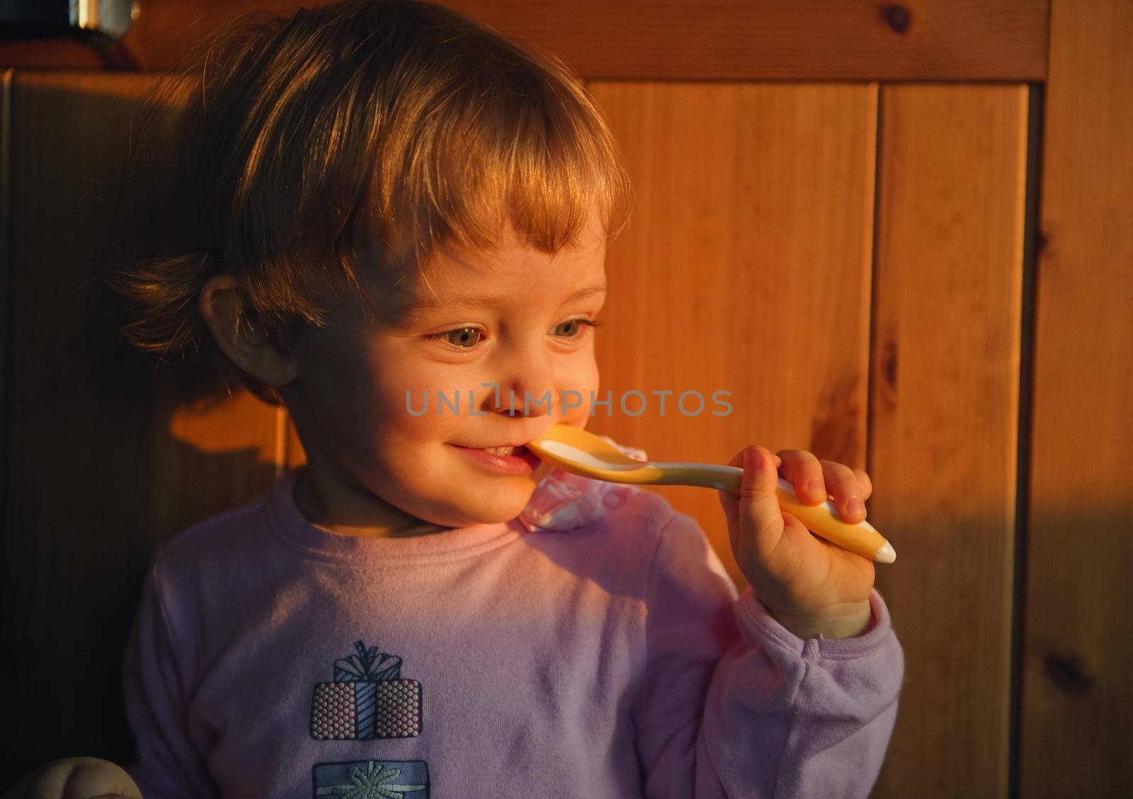 16 months old adorable little baby girl having fun while eating. Illuminating the coming sun 
