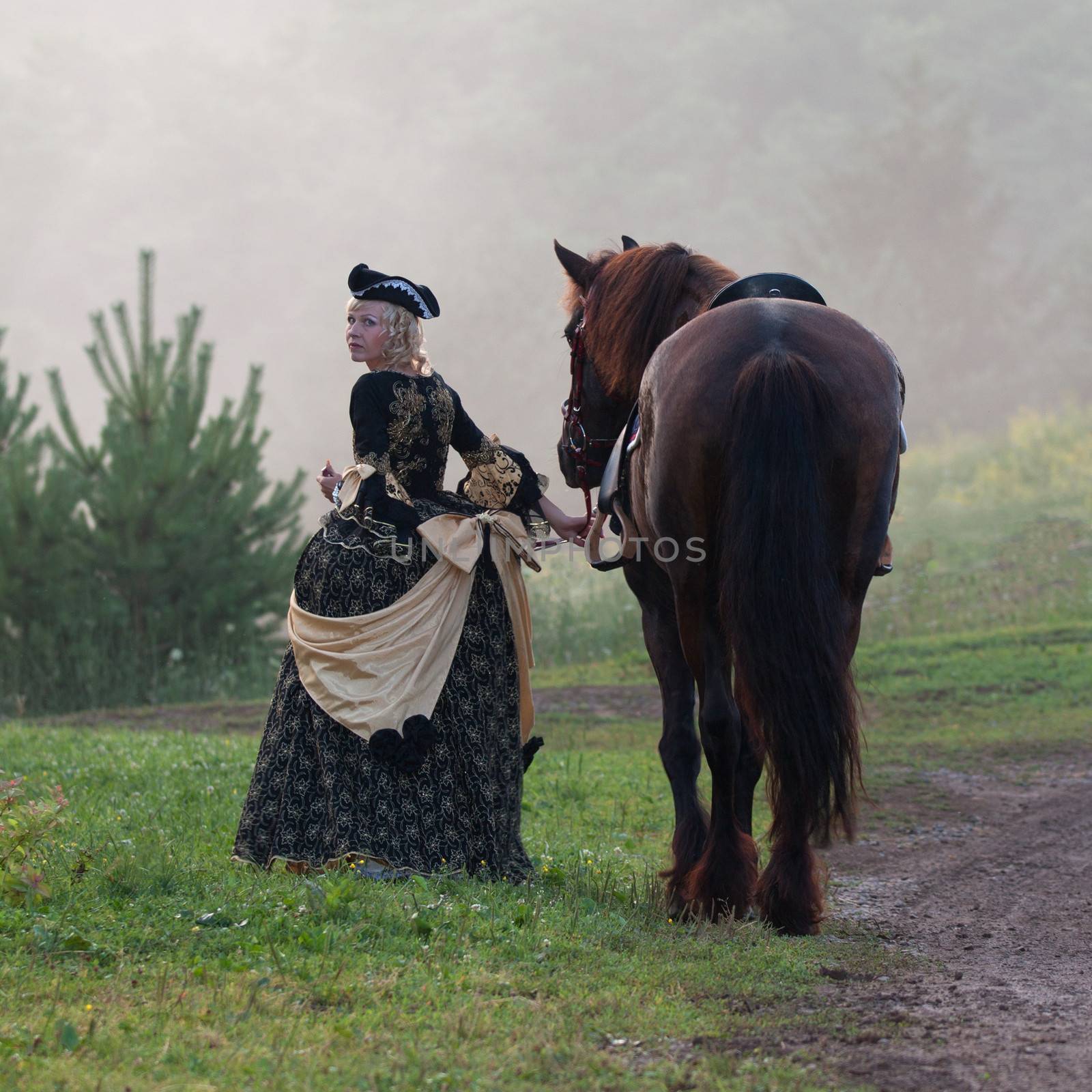 Woman in royal baroque dress, walking beside a horse in the fog
