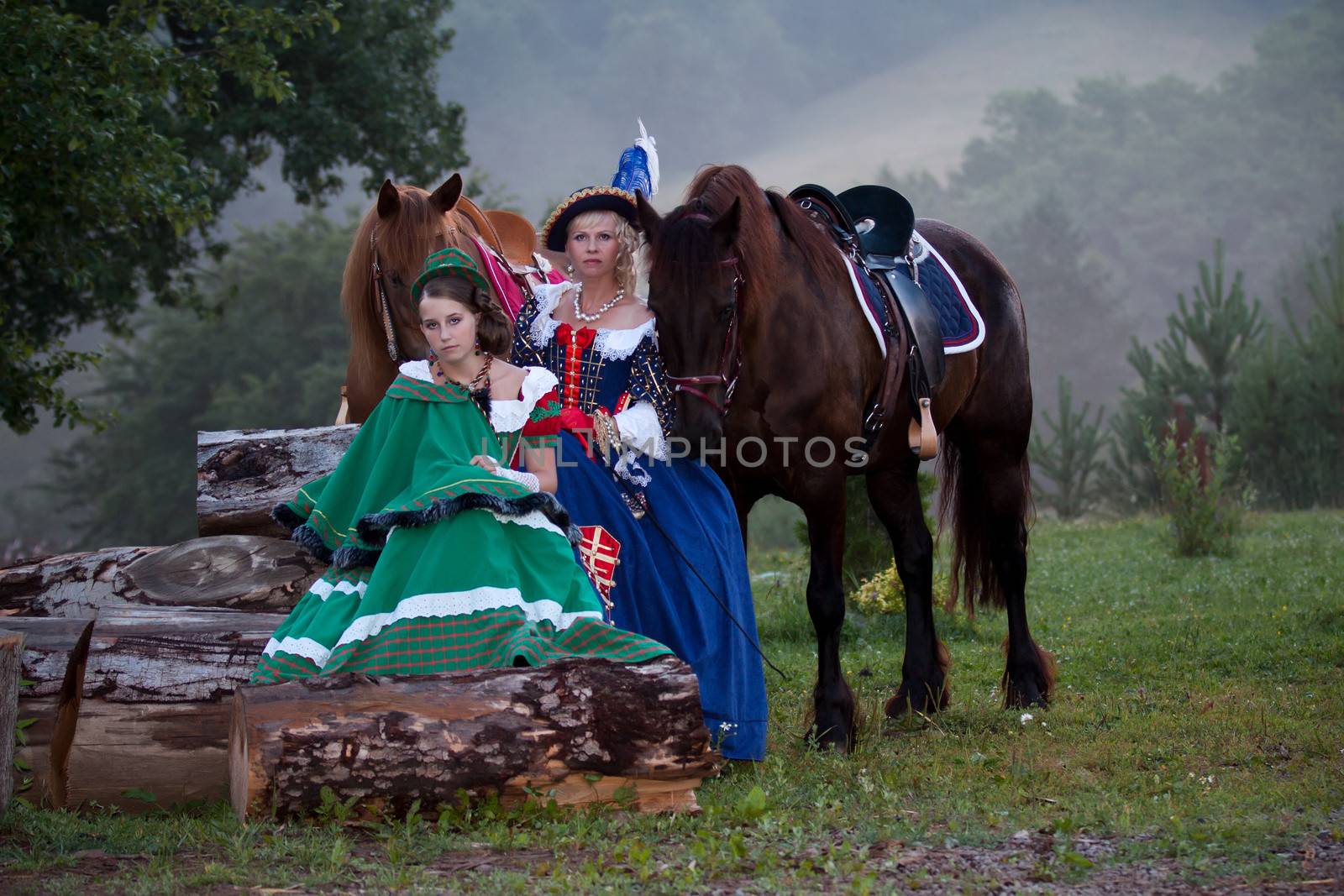 Two women in the royal baroque dress, sitting next to the horses in the fog