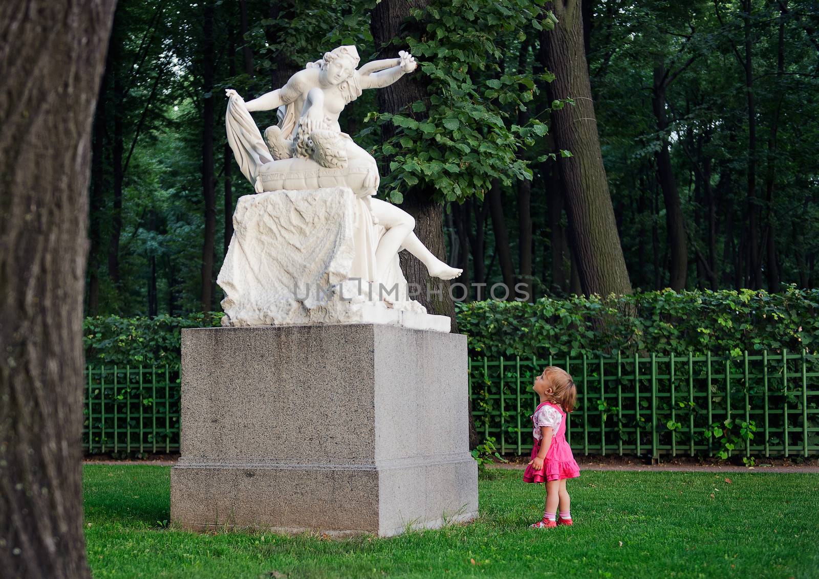The little girl with astonishment looks at a sculpture of "Cupid and Psyche" in old park "Summer garden" in St.Petersburg, Russia 