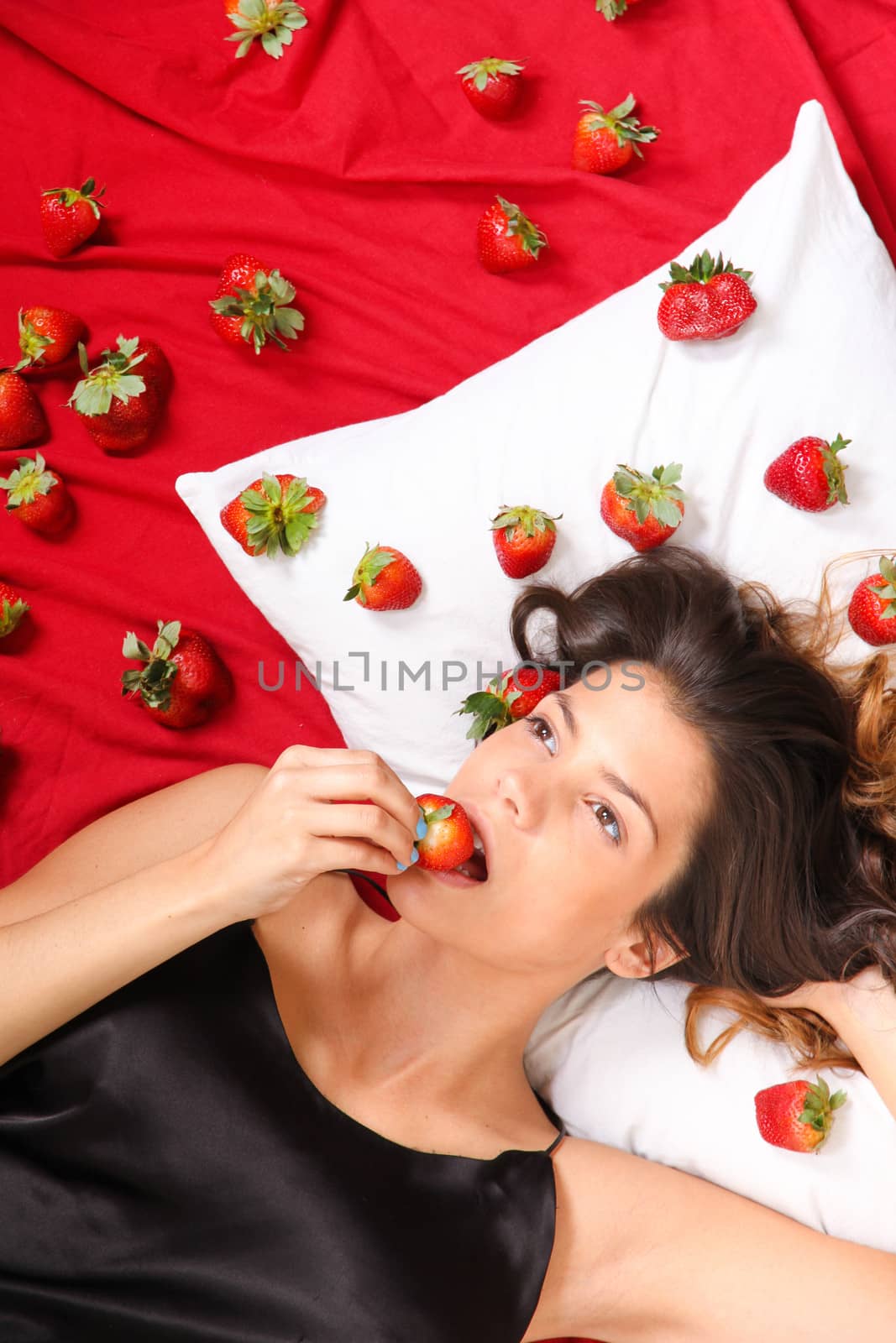 Beautiful, latin Woman eating a Strawberry in bed.
