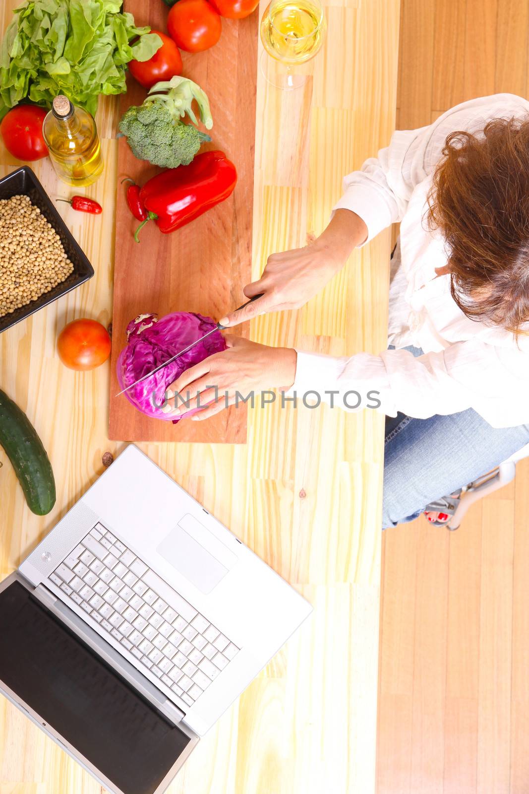 A beautiful mature woman cutting in the kitchen with the help of a computer.