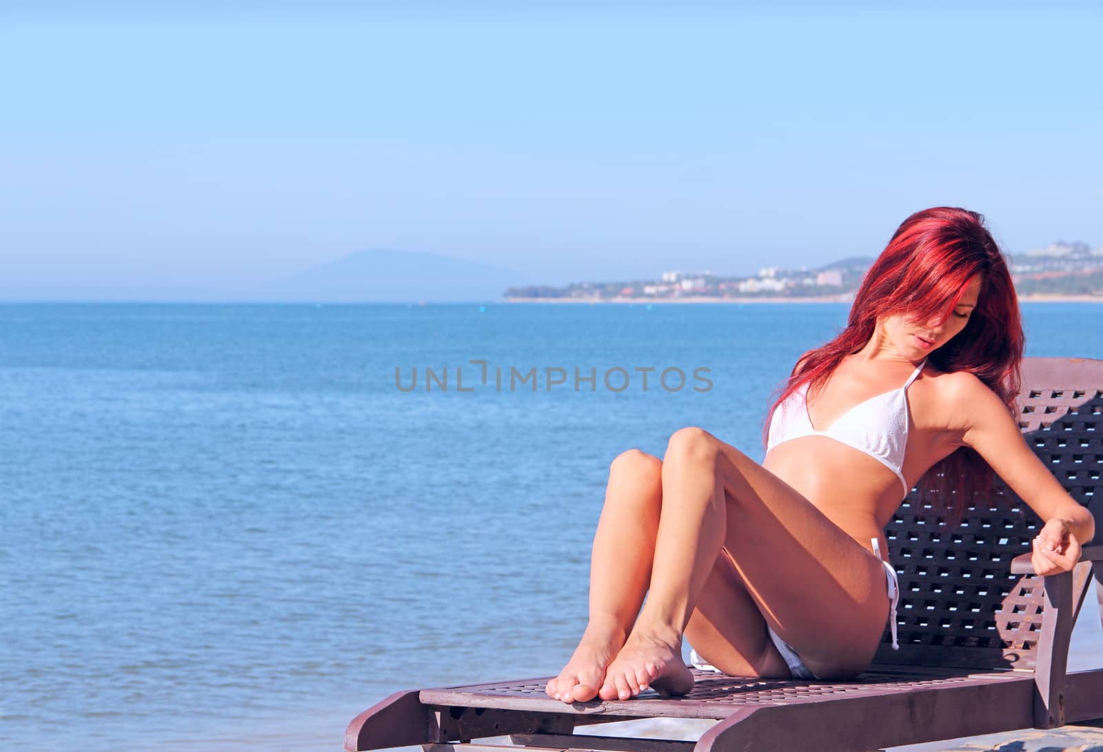 Young woman sitting on chaise lounge at the beach