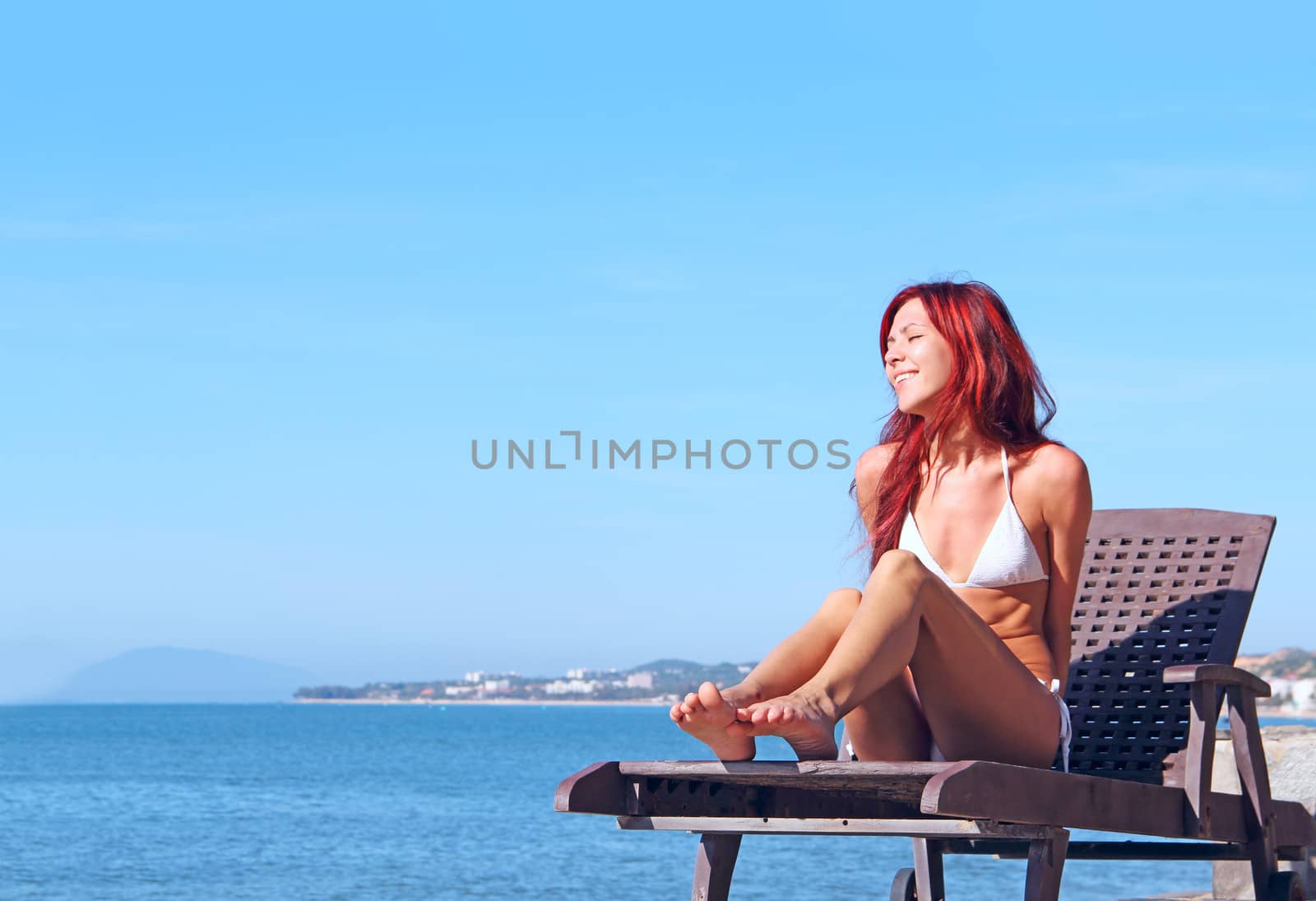 Young woman sitting on chaise lounge at the beach