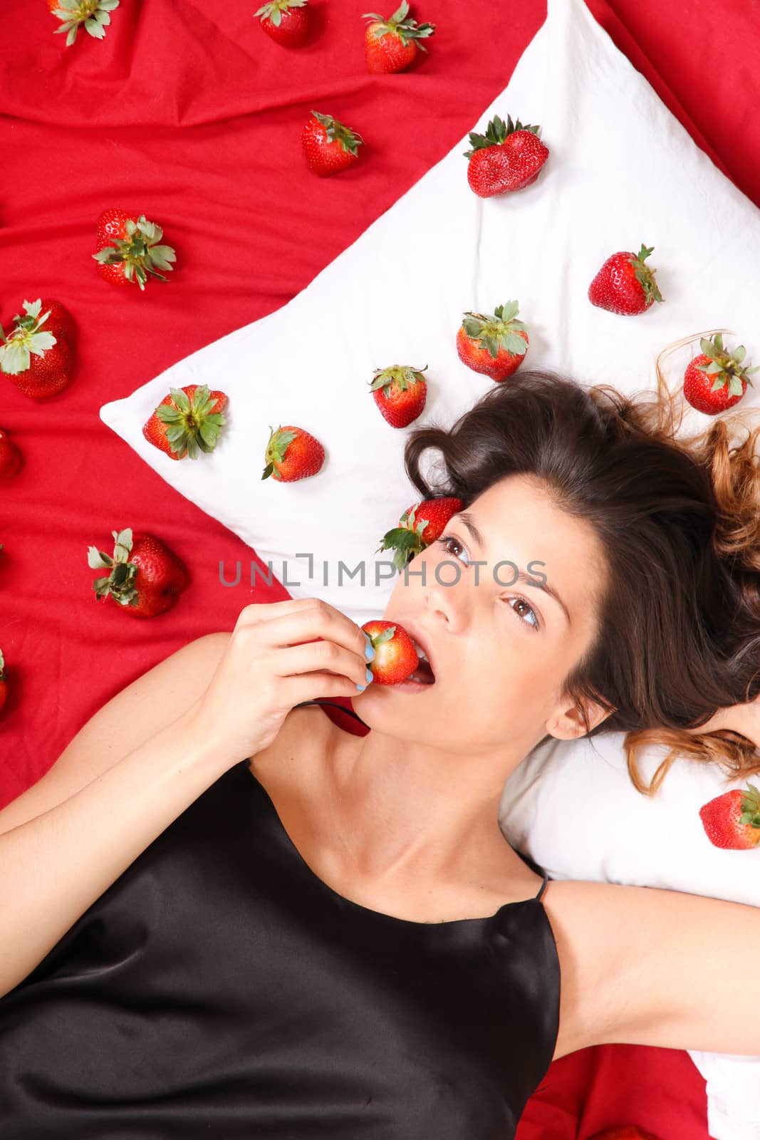 Beautiful, latin Woman eating a Strawberry in bed.

