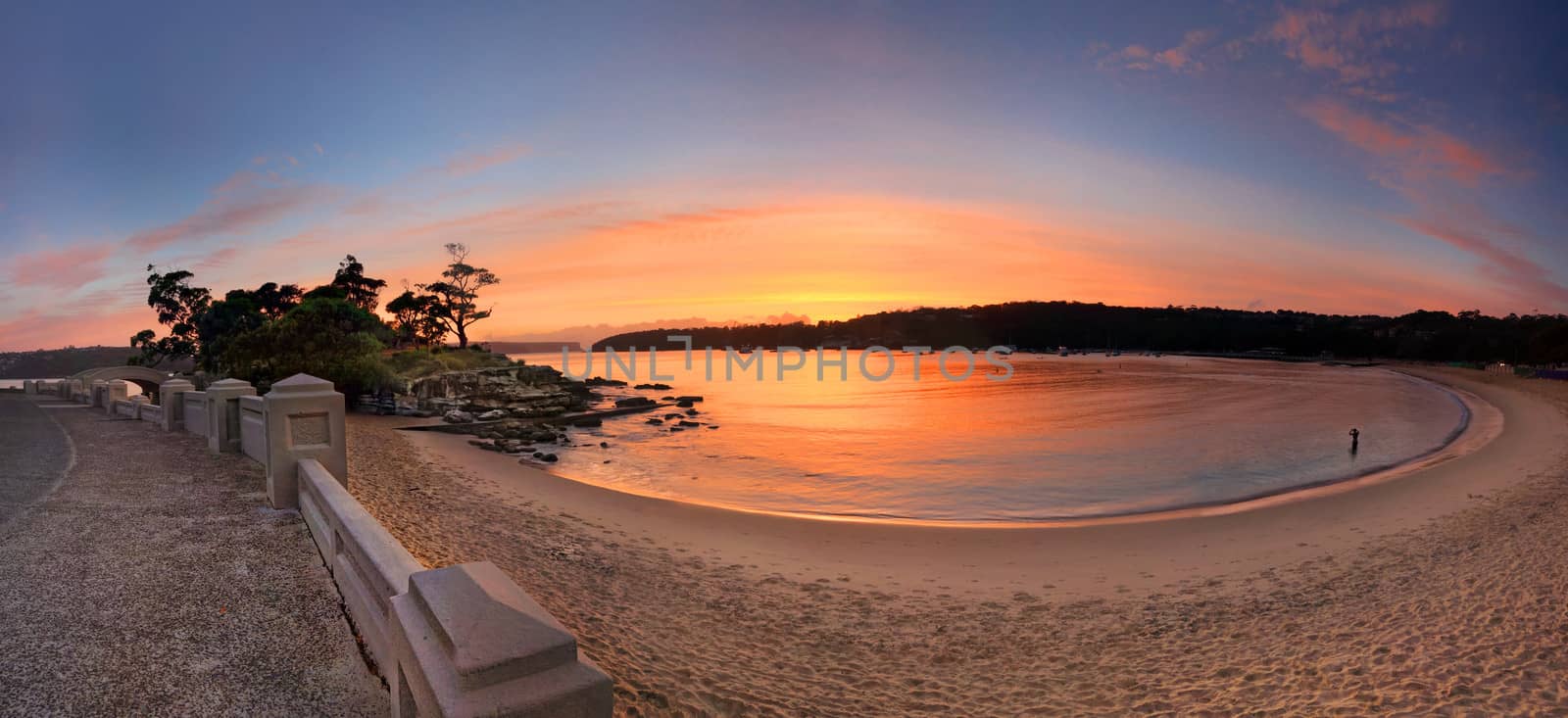 Sunrise at beautiful Balmoral Beach, Mosman, Sydney, Australia, with Rocky Point Island to the left which is accessed by the stone arch bridge. You can see the heads in the very far distance.    Please note this is a stitched panorama taken just before sunrise and the difficulty with this one was the waves constantly breaking at shoreline.
