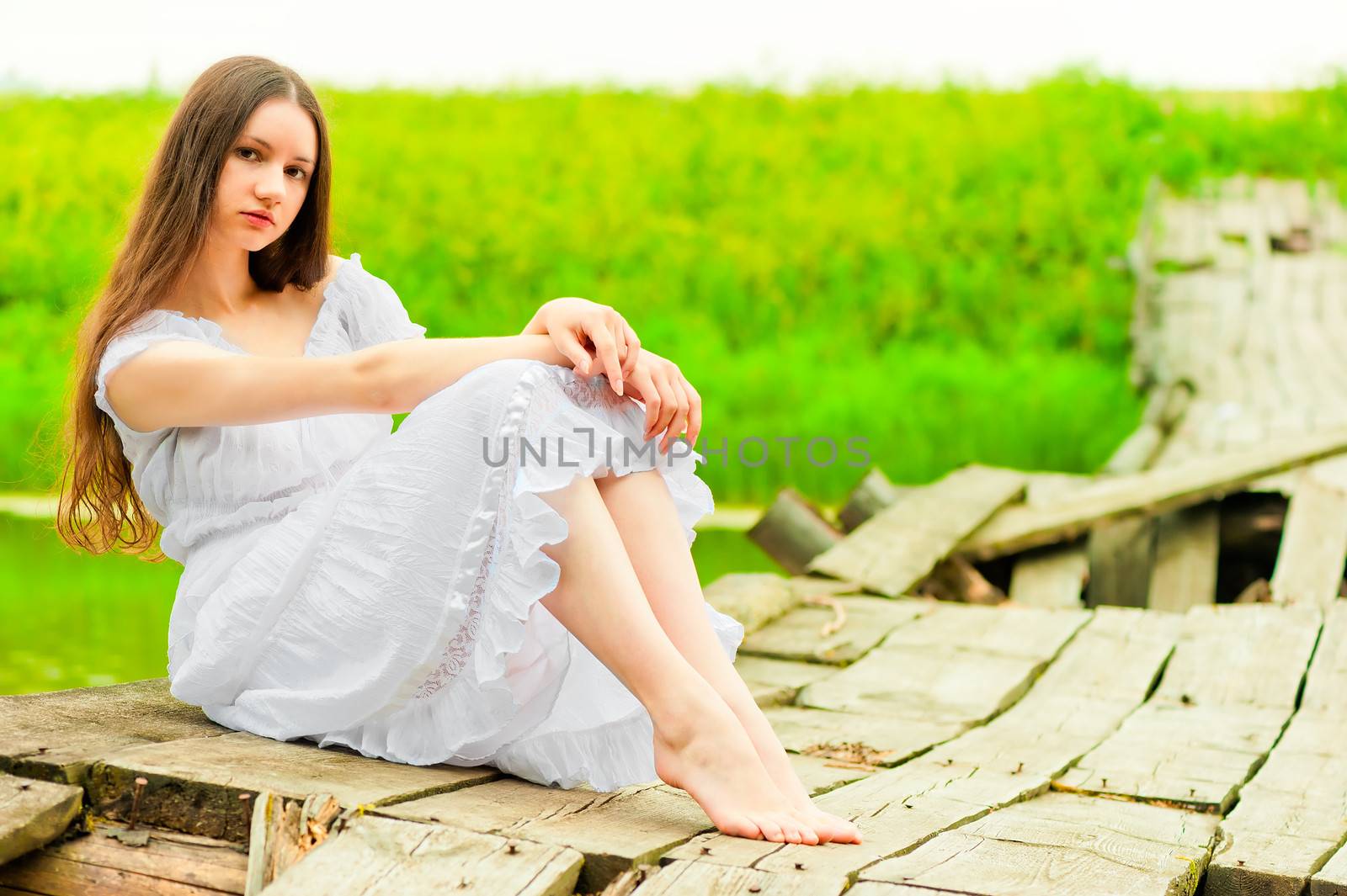 beautiful girl sits on an old wooden bridge