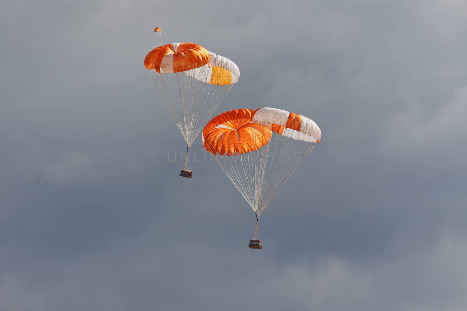 Freights on color parachutes go down the earth against cloudy sky