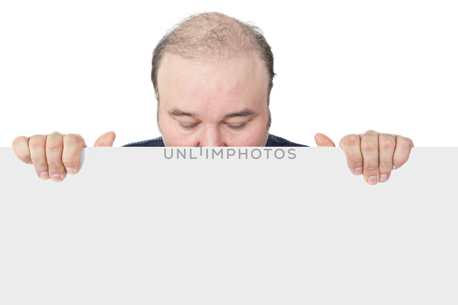 Businessman holding a blank white sign suitable for advertising looking down with closed eyes and hiding his face behind the board in an effort not to have to issue an endorsement