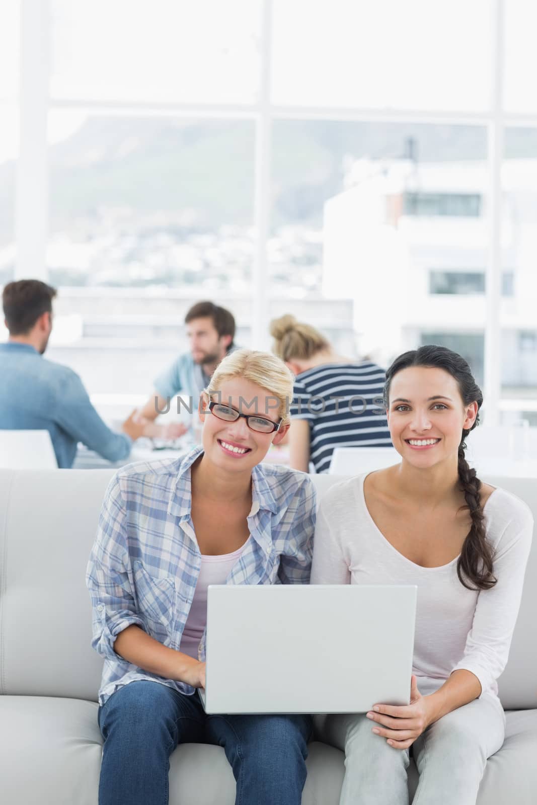 Young women using laptop with colleagues in background at a creative bright office